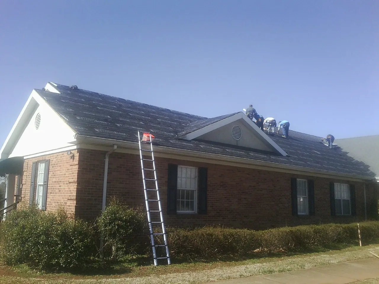 Crew tearing shingles off a brick ranch roof with a ladder set — Emergency Roof Repair work by our crew in Redkey