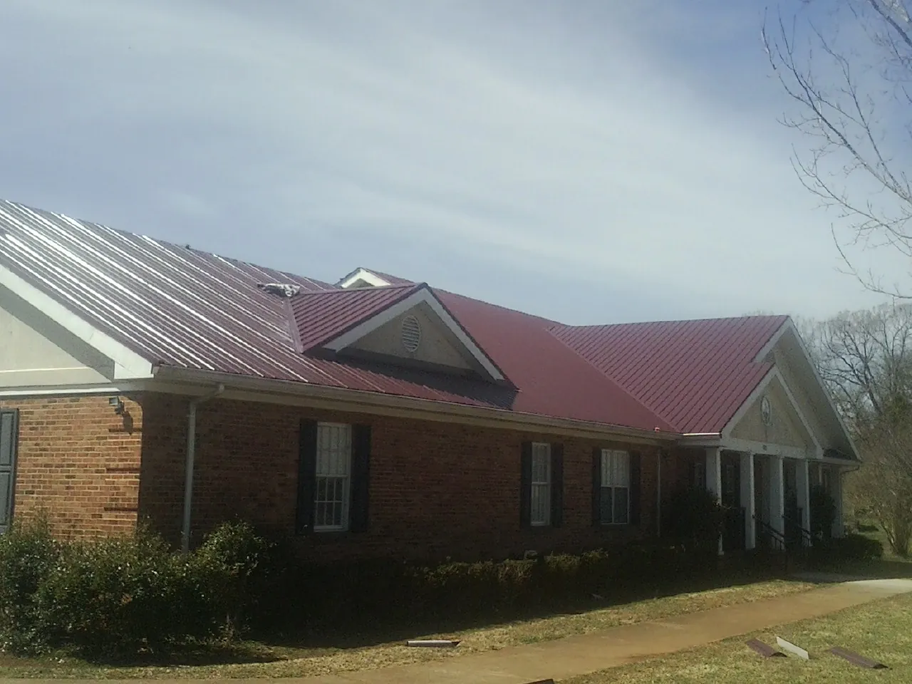 Red metal roof with gabled entries on a long brick building, from a Hail Damage Roof Repair job in Redkey