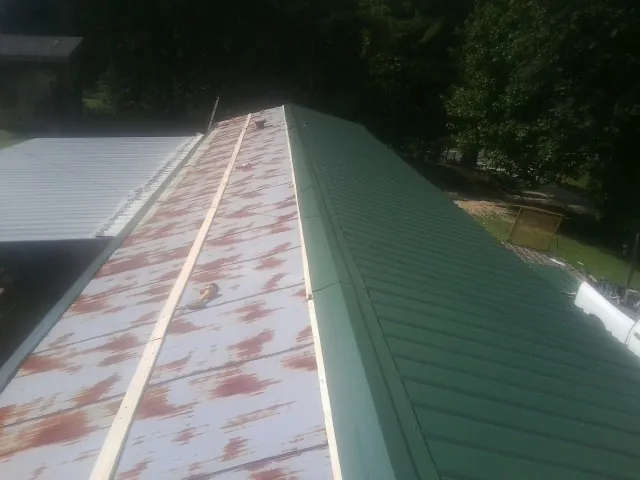 Old rusted panels beside newly installed green metal roofing — Wind Damage Roof Repair by Roofing Brothers in Redkey