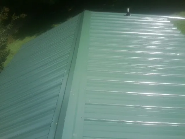 New green metal panels meeting at the ridge of a roof — Flat Roof Repair work by our crew in Redkey