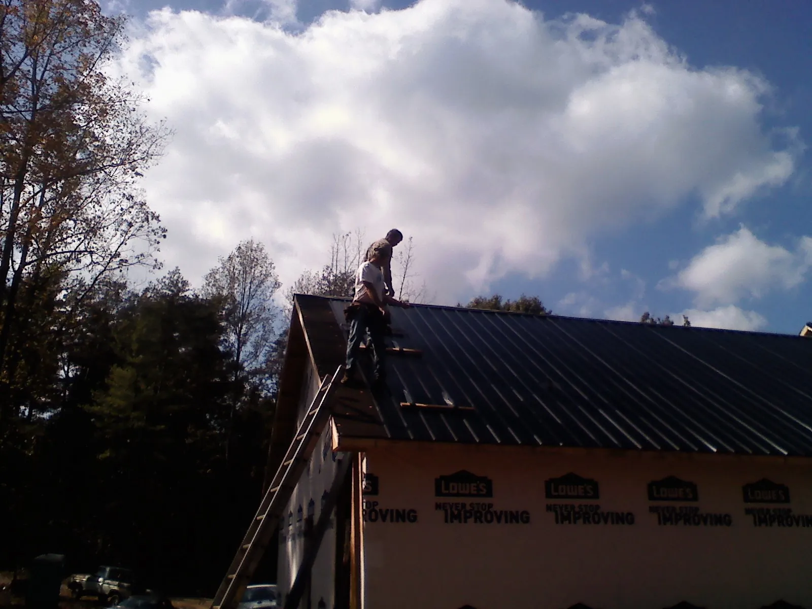 Roofer fastening dark metal panels high against a cloudy sky, from a Roof Inspection job in Redkey