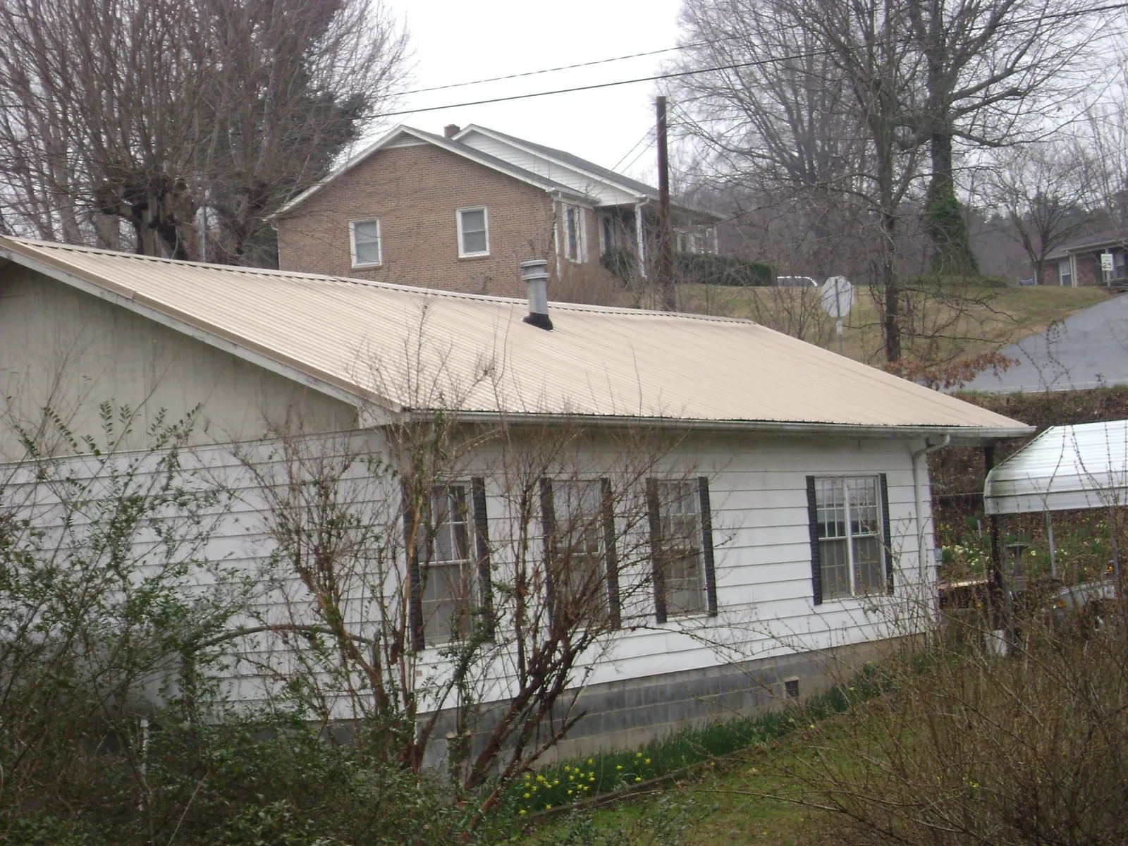 Tan metal roof on a white sided house set into a hillside — Commercial Roofing by Roofing Brothers in Redkey